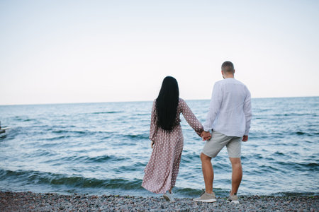 Rear view of a couple walking on the beach, holding hands.の写真素材