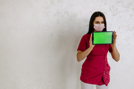 Beautiful Asian woman doctor showing the empty screen tablet and pointing her fingers to the screen close up, Empty green screen tablet background.の写真素材