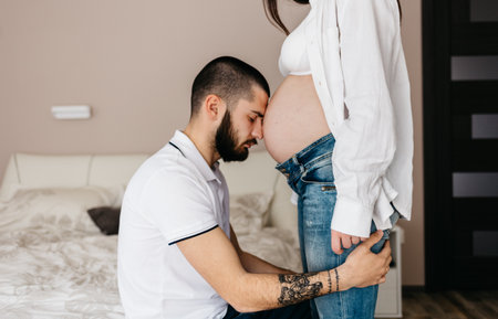 Handsome man is listening to his beautiful pregnant wife's tummy and smilingの写真素材