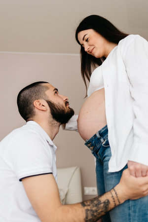Handsome man is listening to his beautiful pregnant wife's tummy and smiling