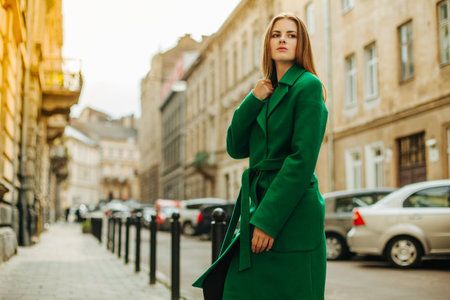 Young beautiful woman in a dark green coat against a background of a residential area. A girl with long hair in glasses on a walk in the city. street autumn fashion. natural beauty womenの写真素材