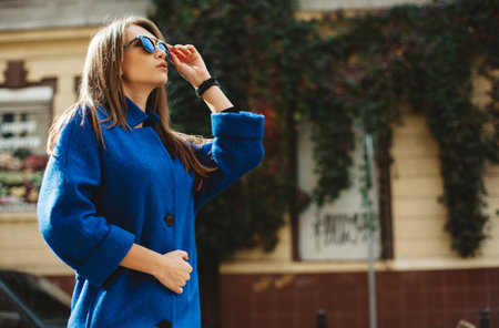 young beautiful stylish woman walking in street in blue coat, autumn fashion trend.の写真素材