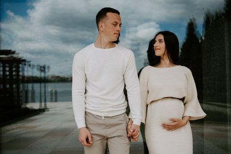 Happy couple: a young beautiful pregnant wife in a long dress and husband walking together on a sunny summer day. Man and woman in love.の写真素材