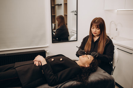 Permanent make-up for eyebrows of beautiful woman with thick brows in beauty salon. Closeup beautician doing tattooing eyebrow. Professional makeup and cosmetology skin care.の写真素材