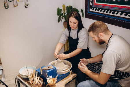 Romantic caucasian couple working on potter wheel. Handsome man and pretty beautiful brunette woman making and sculpting clay pot together and hugging.の写真素材