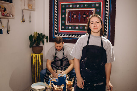 handsome man and happy woman couple in love working on potter wheel while at pottery workshop. husband and wife in the kraft creative studio,young family business shop sculpts pot from clayの写真素材