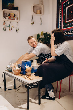 Romantic caucasian couple working on potter wheel. Handsome man and pretty beautiful brunette woman making and sculpting clay pot together and hugging.の写真素材