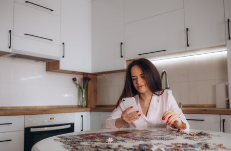 a woman in the kitchen is doing puzzles while holding the phone in her handの写真素材
