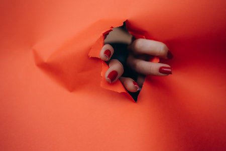 Woman fingers through torn pink or purple cardboard with advertising areaの写真素材