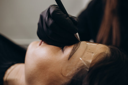 Beautician hand doing brow permanent makeup on an attractive female faceの写真素材