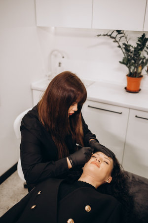 Permanent Makeup For Eyebrows. Closeup Of Beautiful Woman With Thick Brows In Beauty Salon. Beautician Doing Eyebrow Tattooing For Female Face. beauty procedure. high resolutionの写真素材
