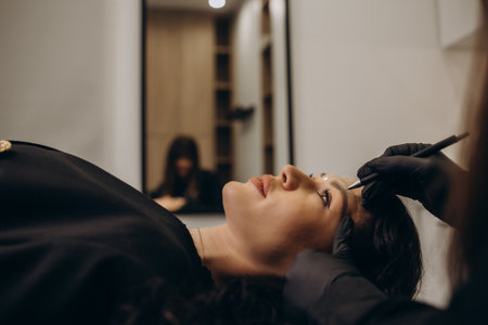 Beautician hand doing eyebrow permanent makeup on a pretty woman faceの写真素材