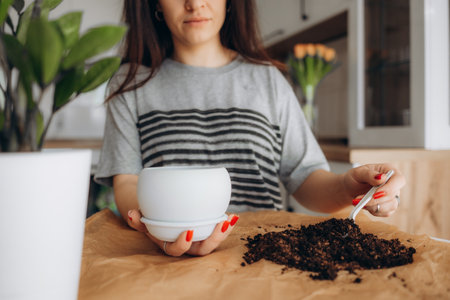 people, gardening and housework concept - happy woman in gloves planting pot flowers at homeの写真素材
