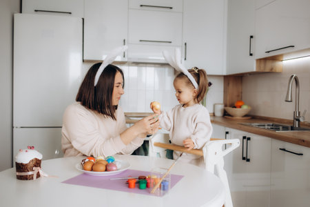 easter, mom and daughter paint Easter eggs with paint, smile and prepare for the holiday at home in the kitchen in the ears of a hare.の写真素材
