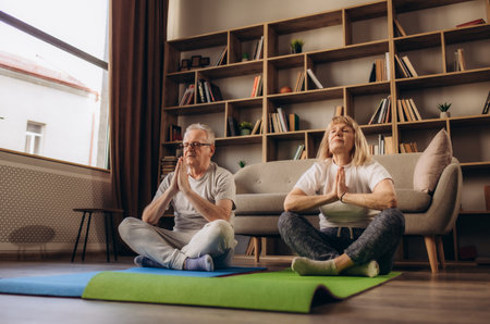 Old elderly senior grandparents spouses couple husband and wife doing sports activity using laptop online tutorial on home fitness. Shaping, keeping fit, doing yoga exercise training on lockdownの写真素材