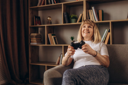 Close up portrait of excited elder grandmother with toothy smile playing video game at studio...