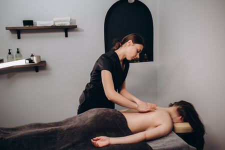 Portrait of a professional female masseuse doing therapeutic massage to her client at the clinic. Concept of relax and body careの写真素材