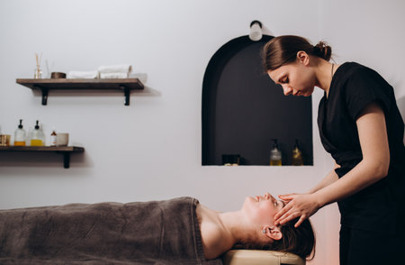 Masseur therapist doing face massage of woman in spa salon, rejuvenating facial massage procedure, healthy skin and body concept. Spa treatments in a beauty salonの写真素材