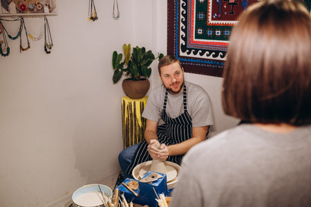 Mid adult couple smiling while doing creative painting on bowls in pottery workshop.