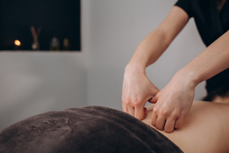 close-up masseur hands doing back massage in spa center. low key photo.の写真素材
