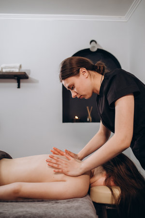 close-up masseur hands doing back massage in spa center. low key photo.の写真素材