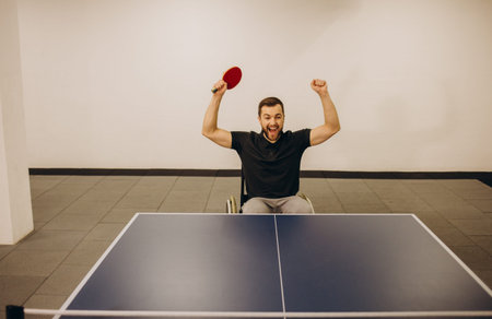 Adult disabled man in a wheelchair play at table tennis with his coach