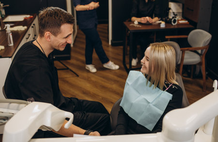 Male dentist in dental office talking with female patient and preparing her for treatment. Explaining the procedure of new dental implants.Rear view of the patient, focus on a dentist.の写真素材