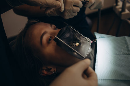 Dentistry at the dentist. Young girl in protective glasses with open mouth. white teeth. Dentist works with photopolymerizer setting seal. treatment of caries. close-up.の写真素材