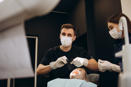 Male dentist in dental office talking with female patient and preparing her for treatment. Explaining the procedure of new dental implants.Rear view of the patient, focus on a dentist.の写真素材