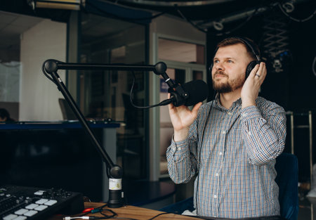 Handsome happy young male radio host broadcasting in studio, using microphone and headphones.の写真素材