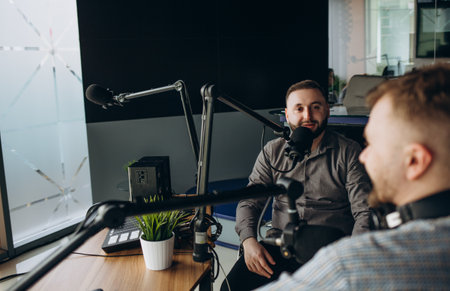 Two college podcasters laughing and having a good time in a studio. Two happy young men co-hosting a live audio broadcast. Two male content creators recording an internet podcast.の写真素材