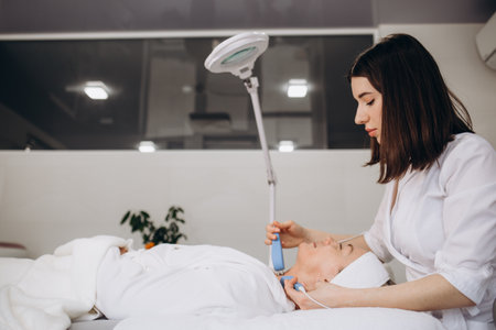A doctor cosmetologist makes a microcurrent facial therapy to a young woman with a device in a beauty wellness salon.Cosmetology and professional skin care.の写真素材