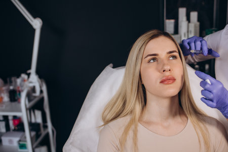 Smile lifting and lip augmentation. Beautician doctor hands doing beauty procedure to female face with syringe. Young woman's mouth counting with filler injection. Marionette lines treatment.の写真素材