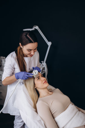 The doctor-cosmetologist makes the Cryotherapy procedure of the facial skin of a beautiful, young...