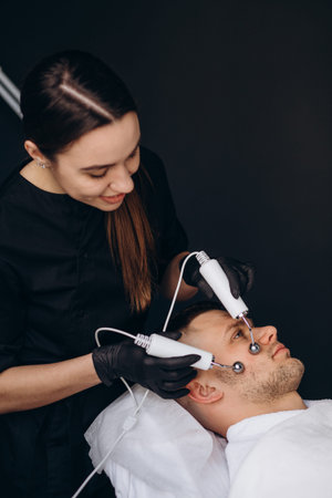 Young man undergoing microcurrent therapy in beauty salon.