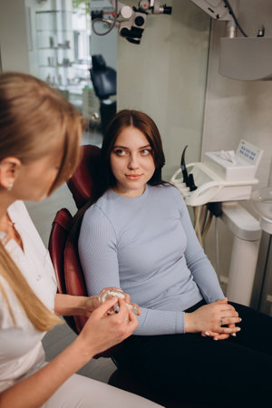 beautiful female dentist holds a model of the jaw and teeth in her hands on which she explains the structure to a girl patient. oral hygiene an example of a jaw in plastic. teeth layoutの写真素材