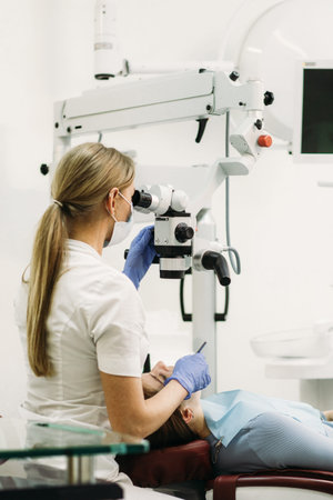 Female dentist using dental microscope treating patient teeth at dental clinic office