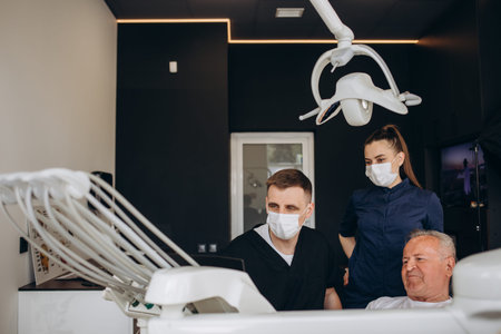 Young dentist and his assistant treating elderly manの写真素材