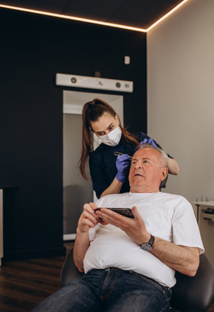 close-up trichologist treats patient, bald mature man with alopecia in hair growth clinic, anti-aging treatments for balding men. concept of hair transplant procedures for men, selective focus.の写真素材