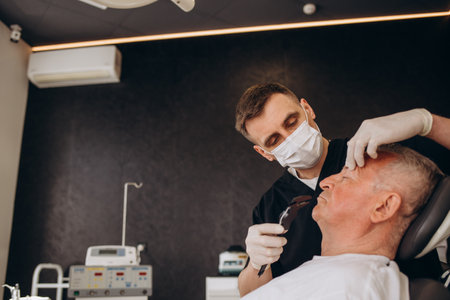 a plastic surgeon measures old senior man's eyelid with a ruler.の写真素材