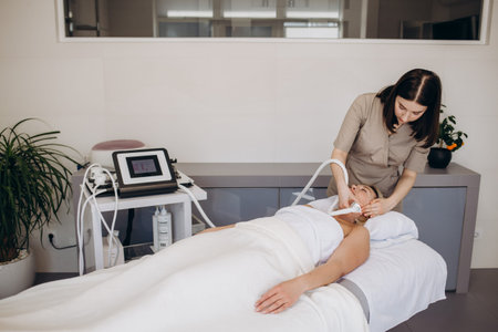 Beautician makes a young beautiful girl a vacuum facial treatment for rejuvenation. Girl is...