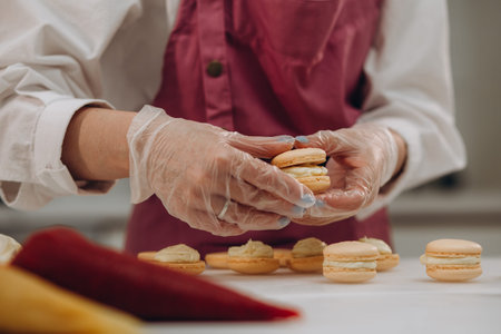 cooking, baking and people concept - chef with confectionery bag squeezing macaron batter or meringue cream to parchment paper at pastry shop kitchen.の写真素材