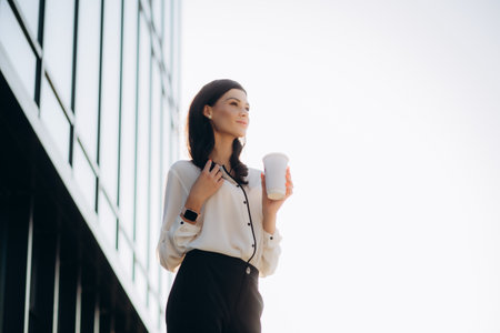 Relaxed stylish businesswoman drinking coffee outside on urban background.の写真素材