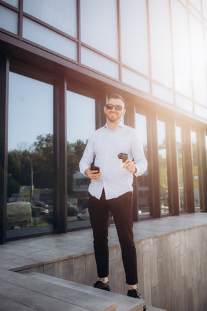 handsome caucasian businessman in a phone call talking and explaining information seriously while using hand gestures, standing on a platform bridge with tall building and busy road in the background.の写真素材