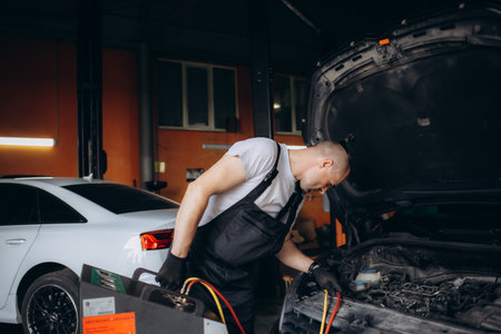 Male car mechanic filling up car air conditioner and check the compressor oil system caused by the car air conditioner is not cold.の写真素材