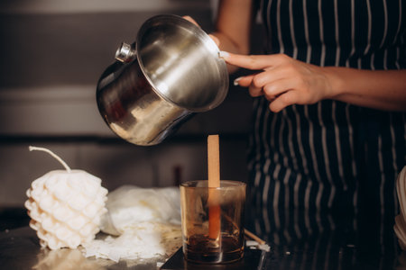 Woman pouring melted wax into amber candles container. Ecological and vegan business. Soya wax candle accessories. Handmade with love. Remote work, online shop, workplace.の写真素材
