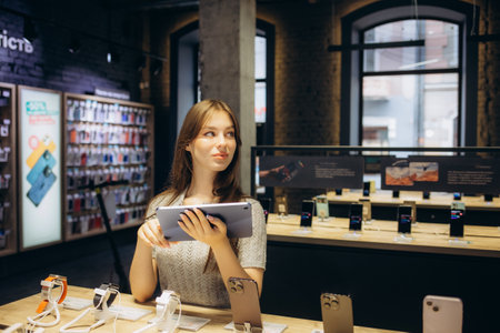Beautiful young woman choosing which digital device to buy in tech store.の写真素材