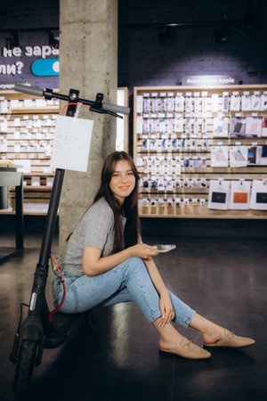 a young girl in a hardware store sits on an electric scooter with a phone in her hand.の写真素材