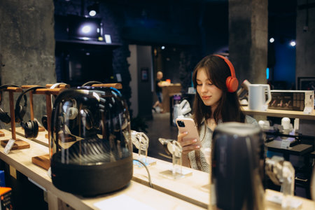 Close up of cute stylish happy girl testing and choosing headphones in a tech store.の写真素材