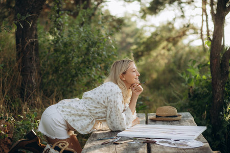 smiling woman outdoors draws a picture on a wooden table.の写真素材